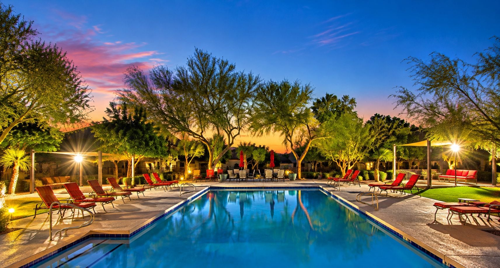 A swimming pool with sunlit lounge chairs and a sunset view.