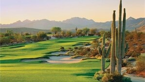 Un parcours de golf avec des cactus et des montagnes en arrière-plan.