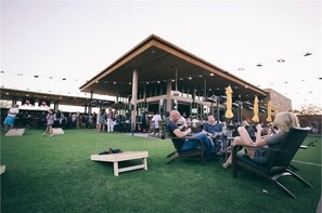 An outdoor seating area with a covered patio, artificial grass, and a building in the background.
