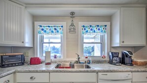 Una cocina con gabinetes blancos, un lavamanos de acero inoxidable, un tostador, un tostador rojo, una cafetera y un lavavajillas.