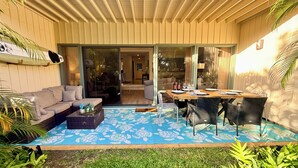 A covered patio with a dining area, a sofa, and a surfboard on the wall. - Poipu Paradise Beach Condo (Koloa)