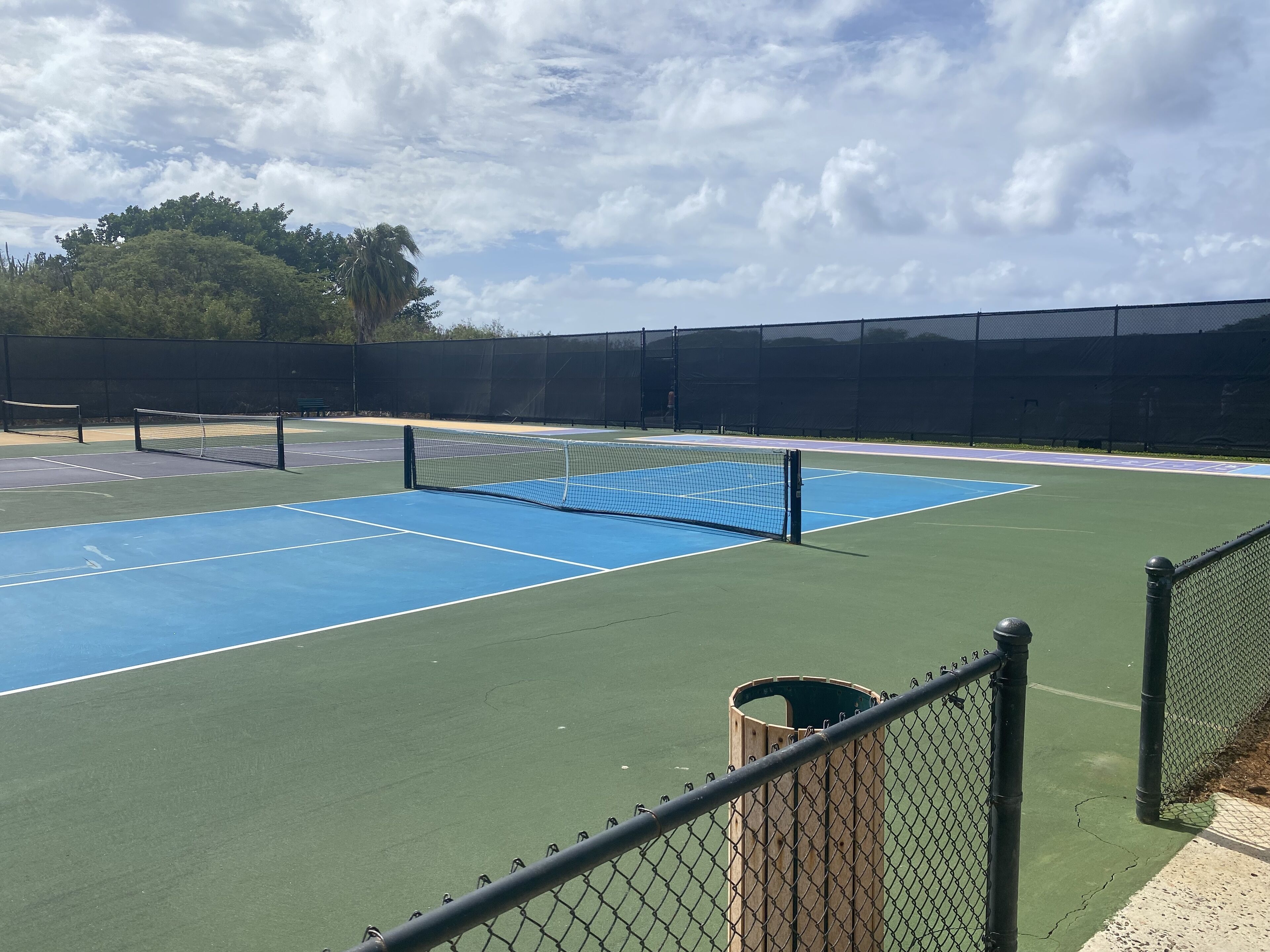 Un terrain de tennis avec un filet, entouré d’une clôture en treillis métallique.
