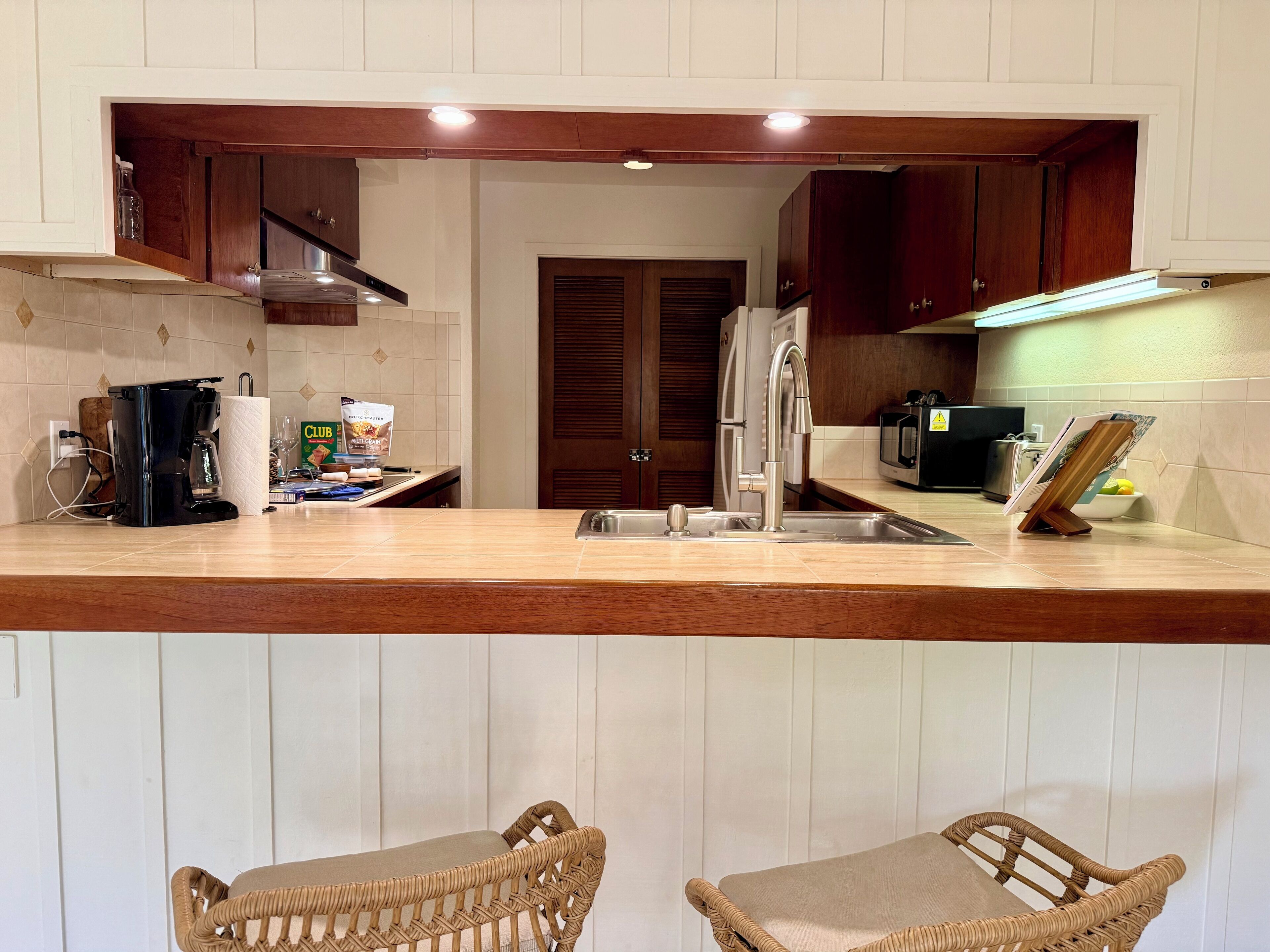 A kitchen with wooden cabinets, a stainless steel sink, a coffee maker, and two wicker chairs.