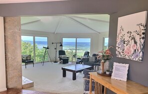 Ein geräumiges Zimmer mit großem Fenster und Blick auf Meer und Grün. Ein Teleskop, ein Schreibtisch und ein Sessel sind vorhanden.