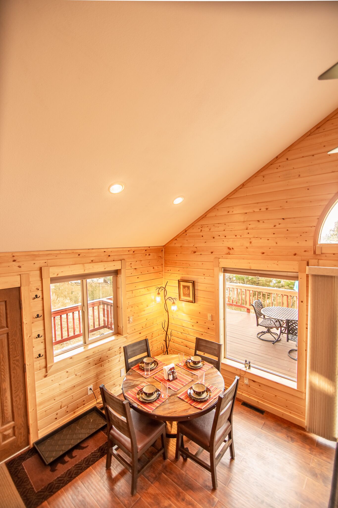A wooden interior with a dining table set for four, wooden walls, and a view of an outdoor deck.