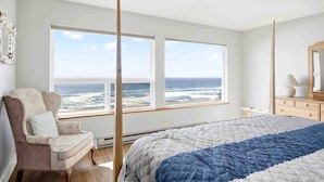 A bedroom with a large bed, a chair, a dresser, and a view of the ocean through large windows. - Stunning Panoramic Ocean Front Views, Single Level, Open Floor Plan, BBQ, Large Deck, Walk to Beach (Cloverdale)