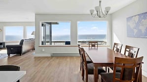 A spacious room with a large dining table, a sofa, and a view of the ocean. - Stunning Panoramic Ocean Front Views, Single Level, Open Floor Plan, BBQ, Large Deck, Walk to Beach (Cloverdale)