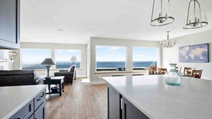 A modern kitchen with a large island, dining area with chairs, and a view of the ocean. - Stunning Panoramic Ocean Front Views, Single Level, Open Floor Plan, BBQ, Large Deck, Walk to Beach (Cloverdale)