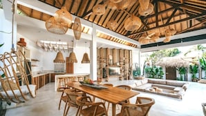 Un vaste espace de vie comprenant une table à manger en bois, des chaises en osier et un grand canapé.