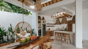 Une cuisine moderne avec un îlot central en bois, des luminaires suspendus en osier et un coin repas comprenant une table en bois et des chaises en osier.