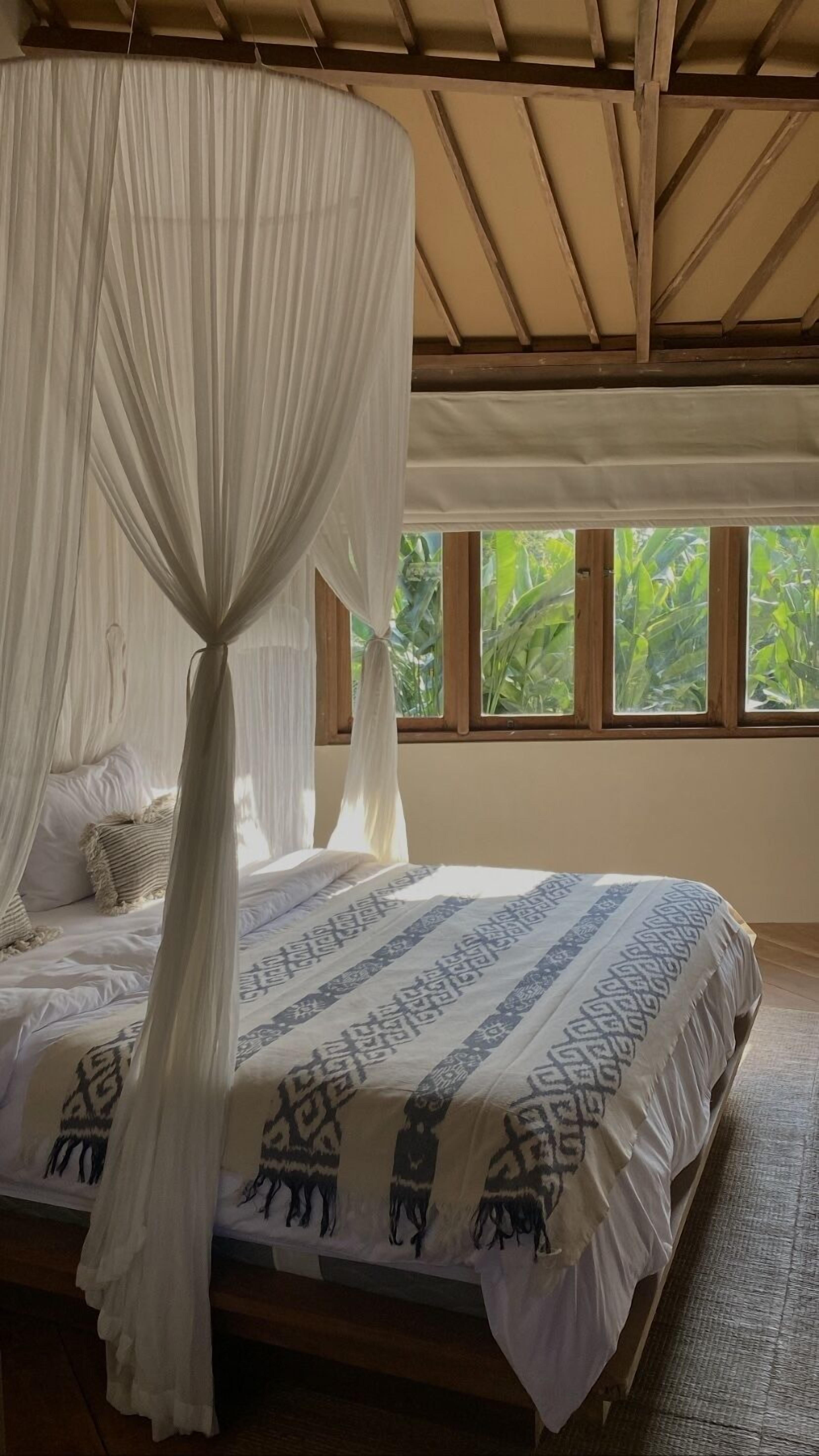 A bed with a canopy, a patterned bedspread, and a view of greenery through windows.