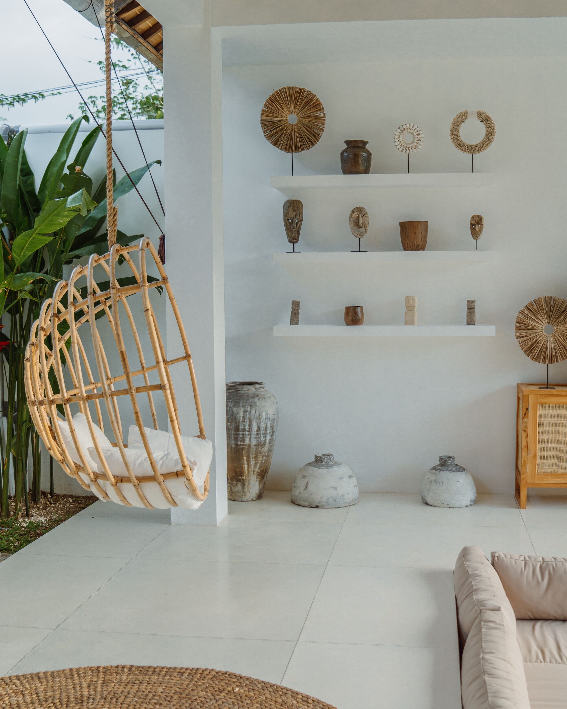 Una sala moderna con un sillón colgante, estantes blancos con adornos y una planta grande.