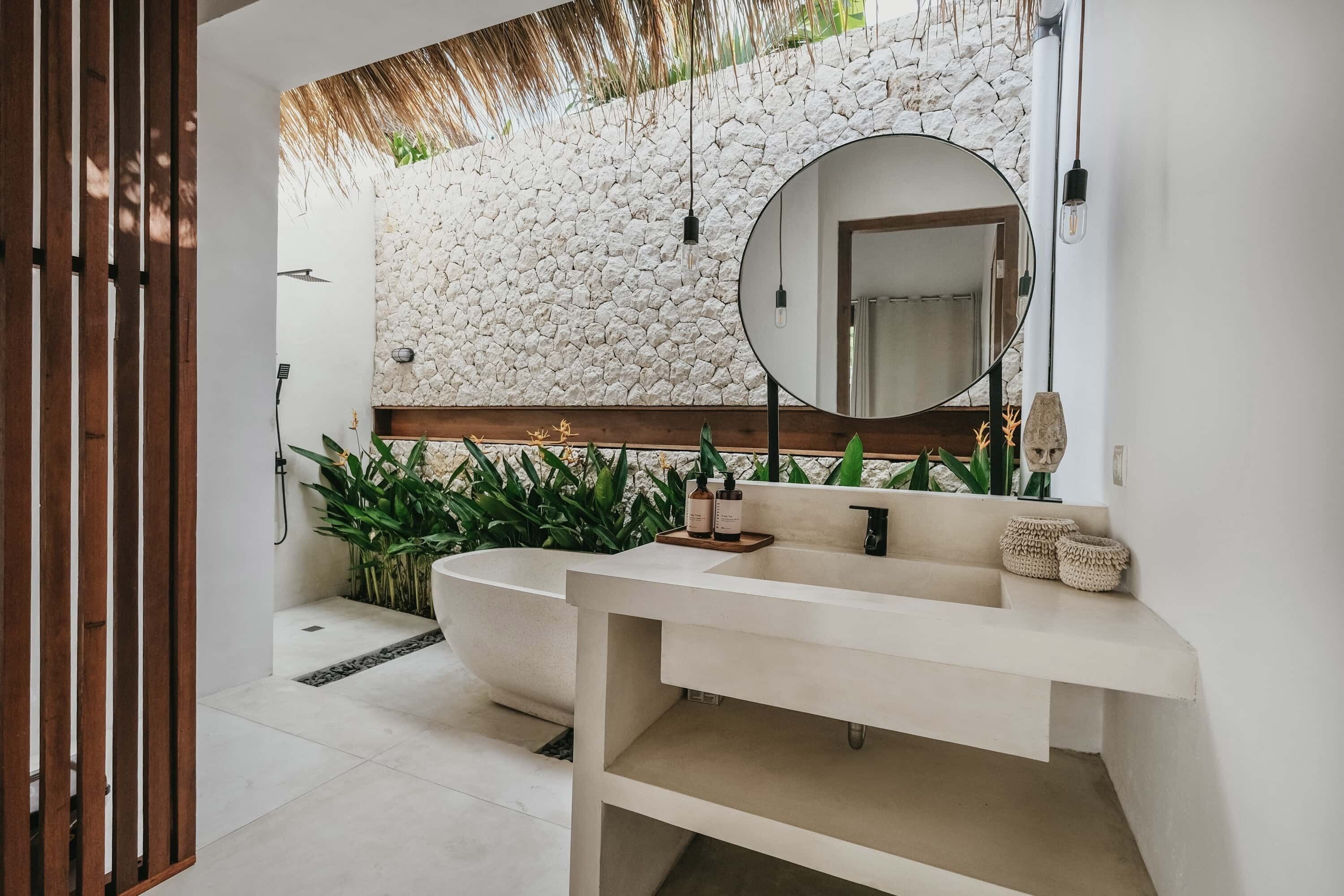 A modern bathroom with a stone wall, a freestanding bathtub, and a round mirror.