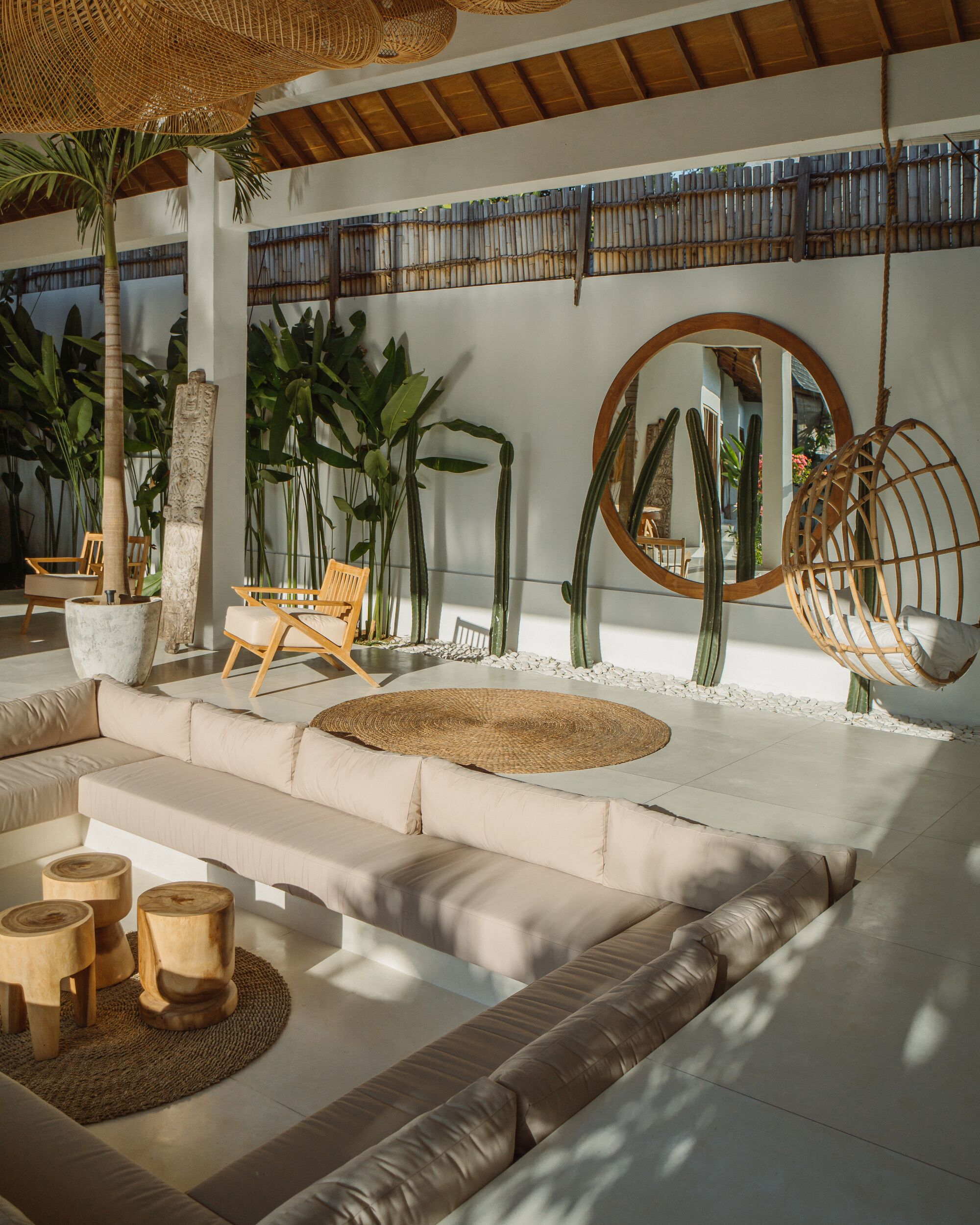 Un espace de détente moderne comprenant un canapé, des chaises en bois, une balançoire suspendue et diverses plantes.