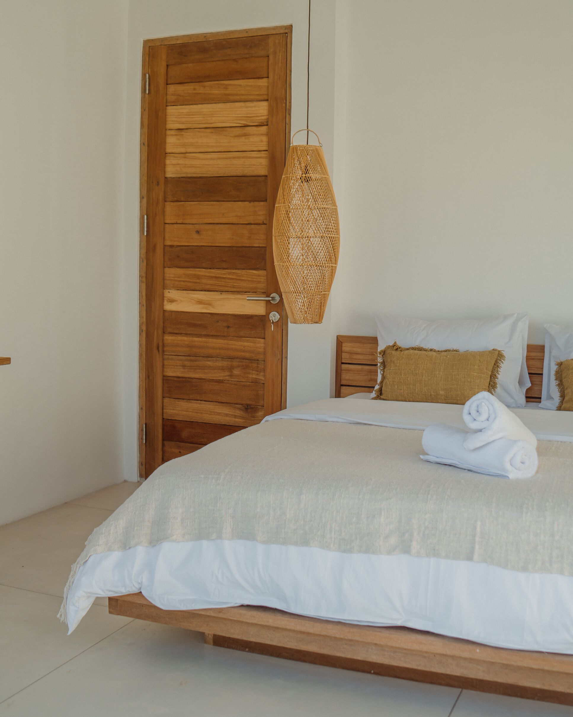 A bedroom with a wooden door, a woven hanging light fixture, a bed with white bedding, and two pillows.