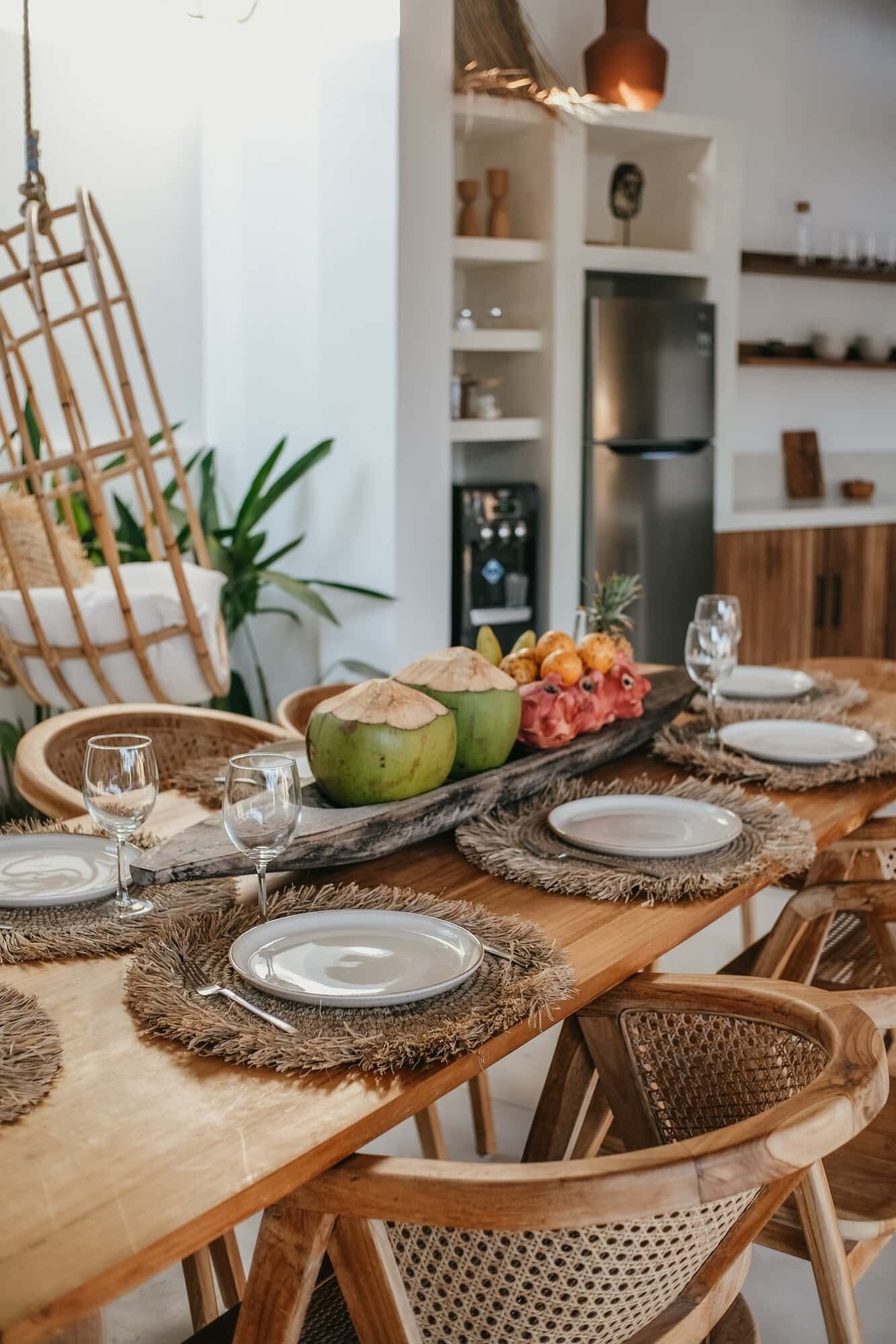 A wooden dining table set with plates, glasses, and a fruit platter.