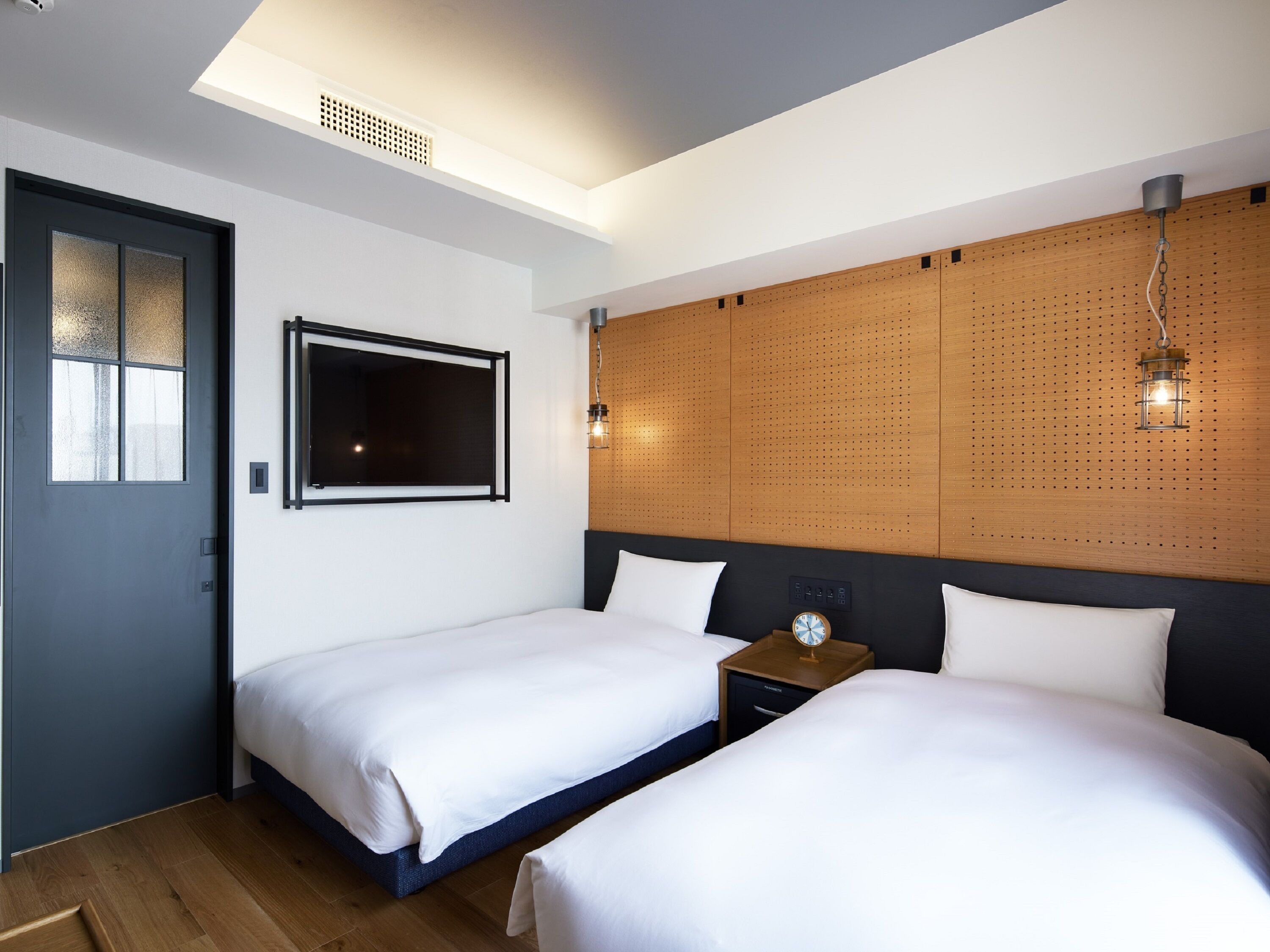 A hotel room with two beds, a large window, a wooden headboard, and a wall-mounted clock.