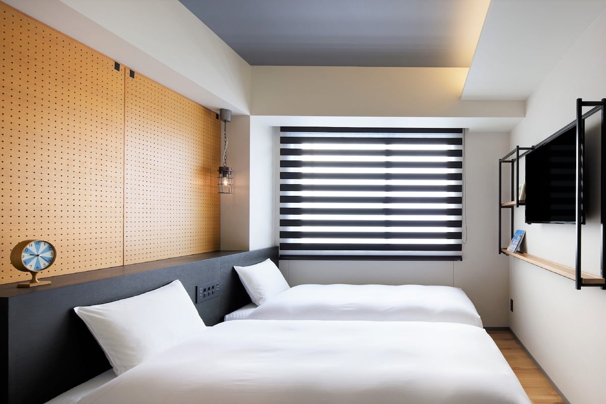 Una habitación de hotel moderna con una cama, un panel de madera decorativo, un televisor montado en la pared y una ventana con persianas.
