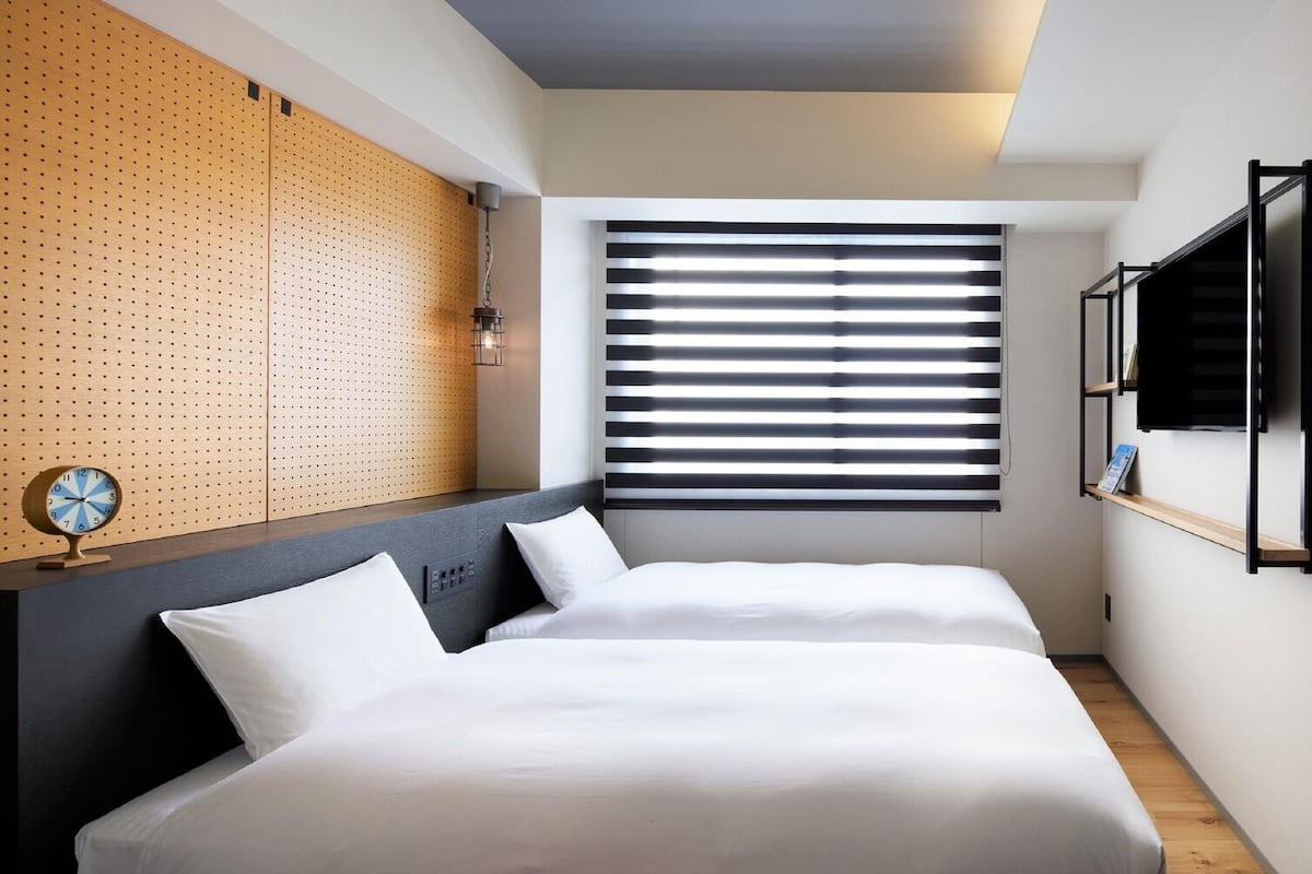 Una habitación de hotel moderna con una cama, un reloj de pared, una ventana con persianas y una pared decorativa de madera.