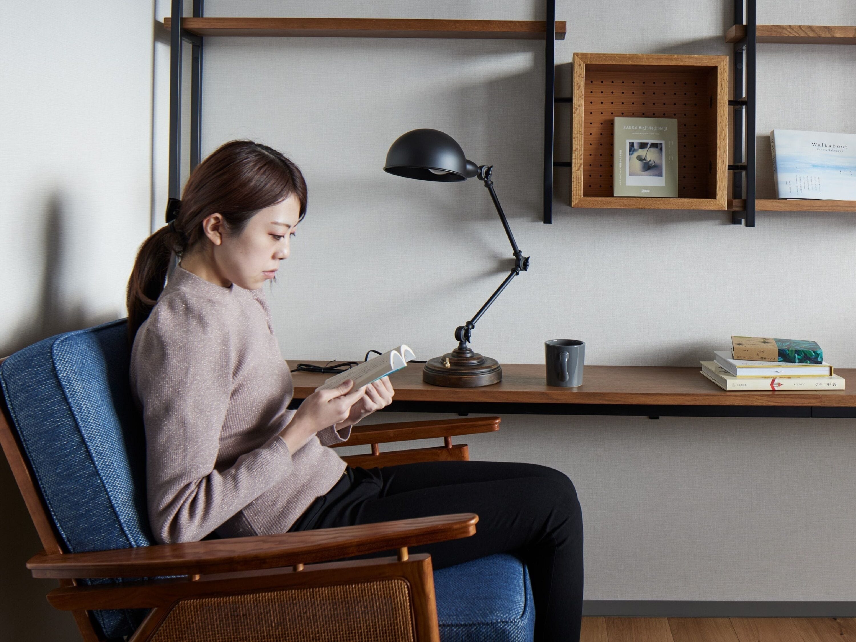 Eine Person sitzt an einem Schreibtisch mit einer Lampe, einer Tasse und Büchern.