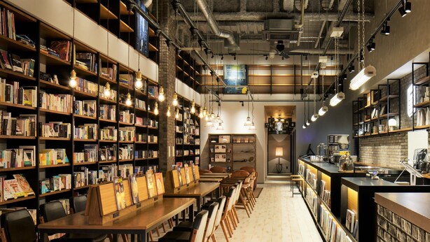 Une librairie avec des tables et des chaises en bois, des étagères et un comptoir où se trouve une machine à café.