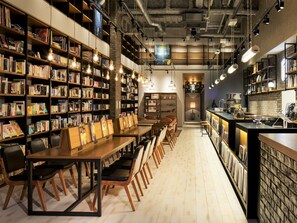 Une librairie avec des tables et des chaises en bois, des étagères et un comptoir où se trouve une machine à café.