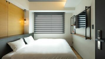 A modern hotel room with a large bed, a wooden headboard, a wall-mounted TV, and a window with blinds.