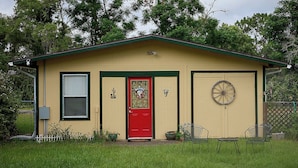 Un petit bâtiment d’un seul étage, avec une porte rouge, une fenêtre avec des stores, un interphone et une poignée de porte en forme de roue.