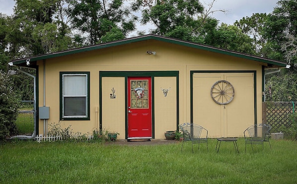 A small, single-story building with a red door, a window with blinds, a doorbell, and a wheel on the door.