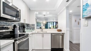 A modern kitchen with white cabinetry, stainless steel appliances, and a view to the outdoors. - Beautifully Updated Beachfront Condo w/Resort Amenities, including Heated Pool & WiFi (Marco Island)