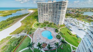 A high-rise hotel with a pool, surrounded by greenery and a view of the ocean. - Beautifully Updated Beachfront Condo w/Resort Amenities, including Heated Pool & WiFi (Marco Island)