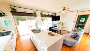 A modern kitchen with a central island, a dining area with a sofa, and a ceiling fan.