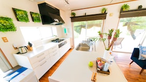 A modern kitchen with white cabinetry, a built-in stove, and a large island with a sink. There are potted plants on the windowsill and a coffee machine on the counter.