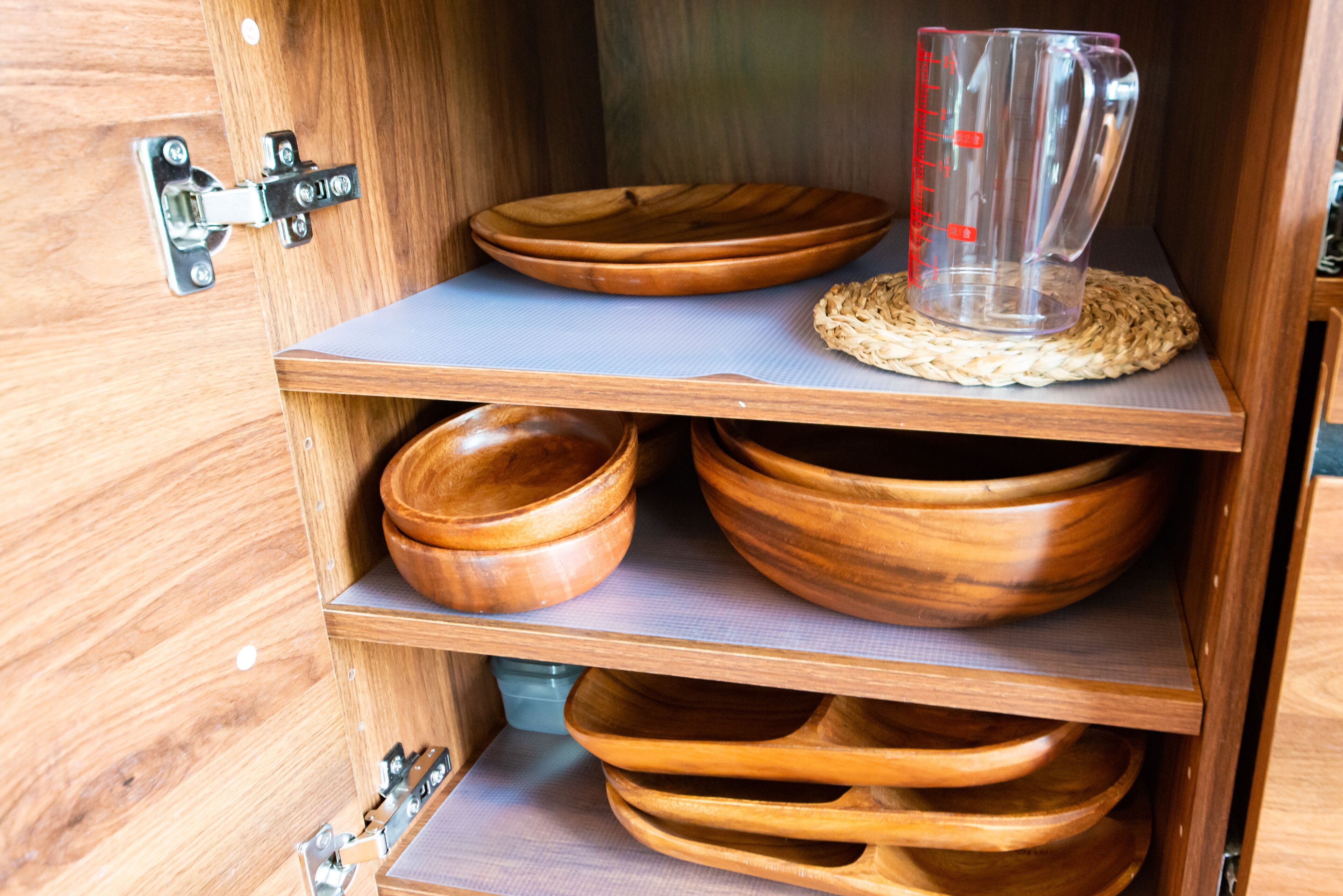 Un armario de madera con varios estantes que contienen cuencos de madera y un vaso medidor transparente.