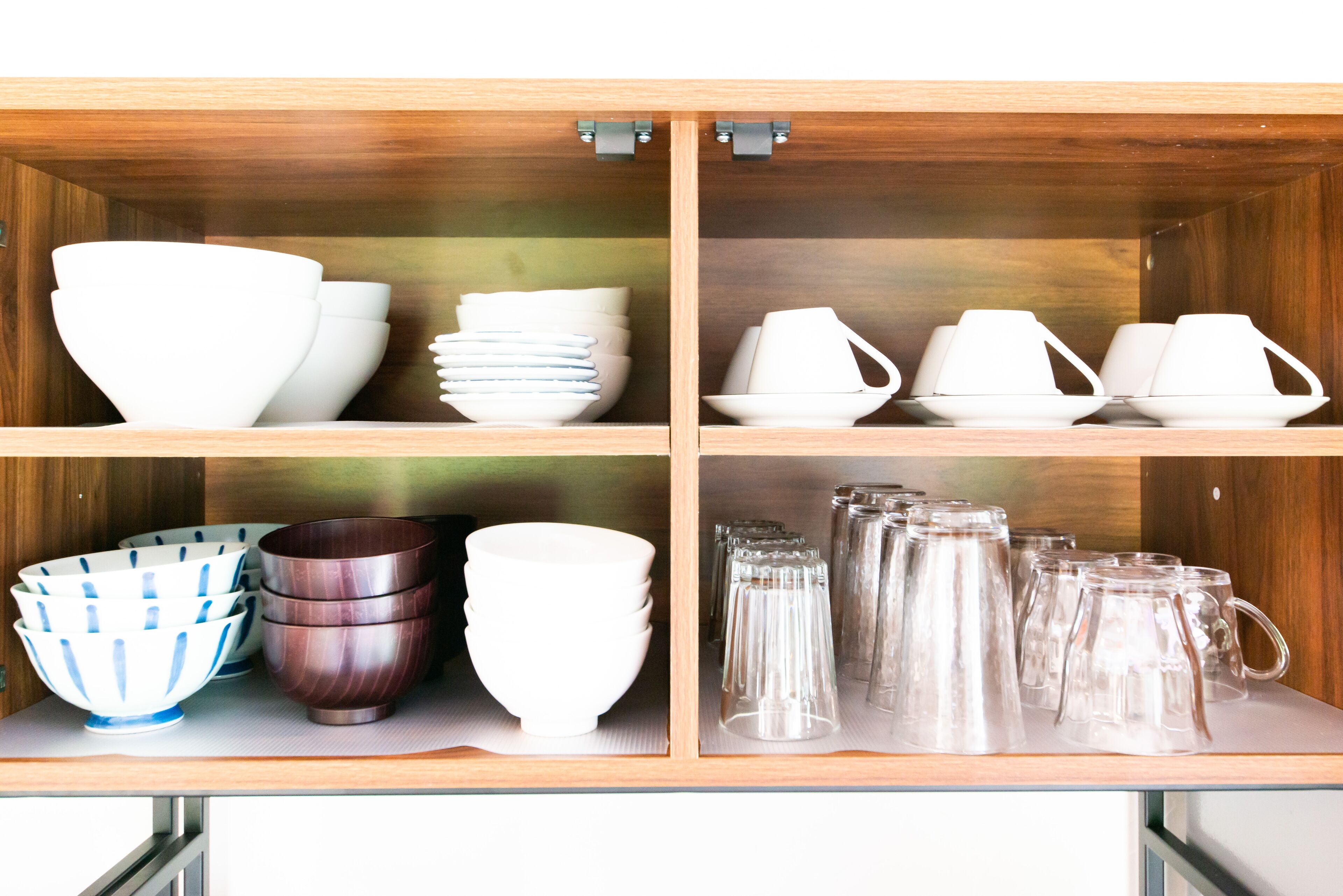 A cabinet with four shelves containing various white and brown bowls, plates, and glass mugs.