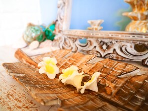 Un plateau en bois orné d’un motif décoratif, deux fleurs blanches et un miroir avec un cadre travaillé.