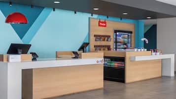 A modern reception desk with a blue wall and wooden accents, a 'Market' sign, and a refrigerated display.
