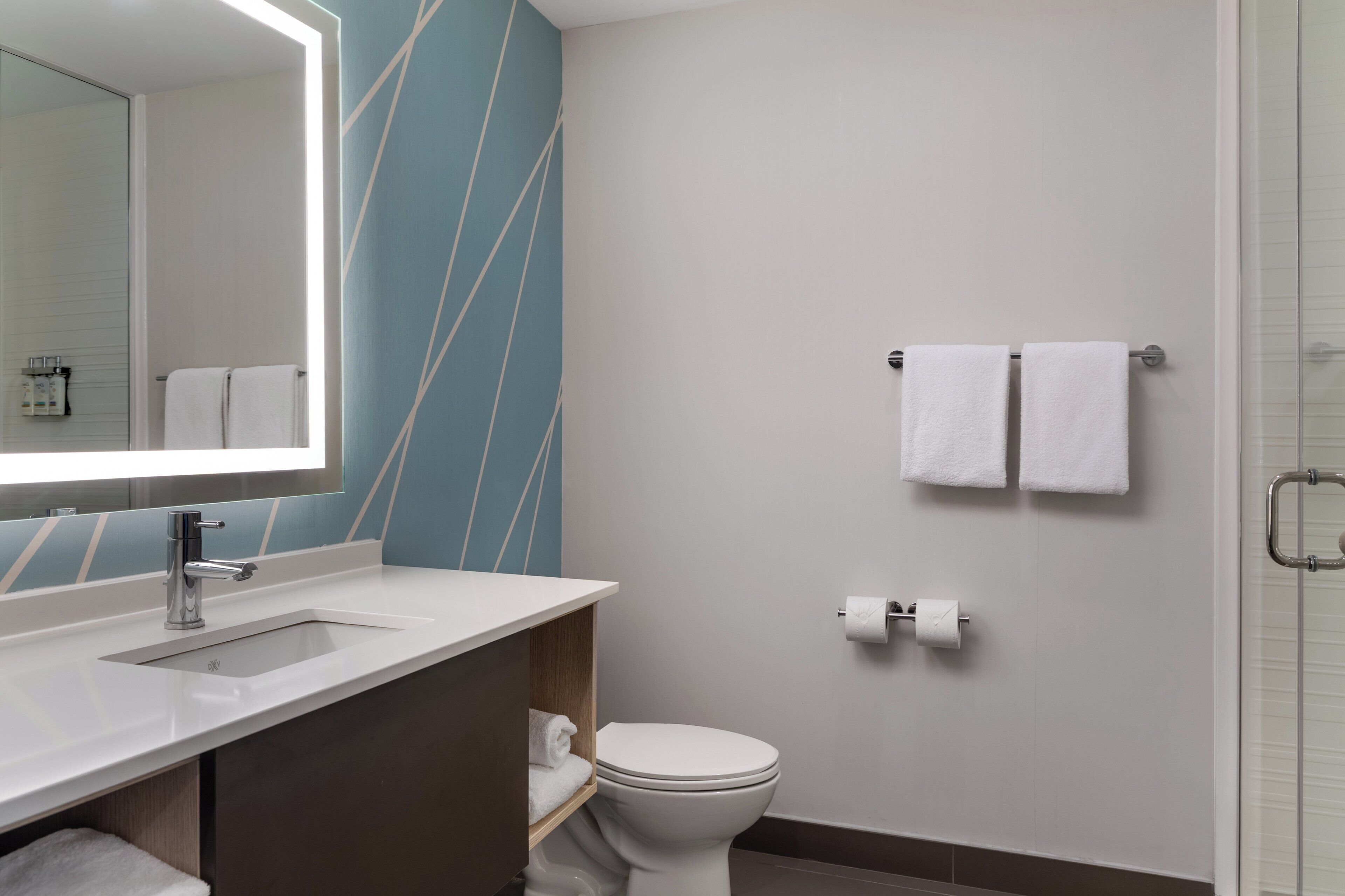 Un baño moderno con lavamanos blanco, un espejo, inodoro y zona de ducha.