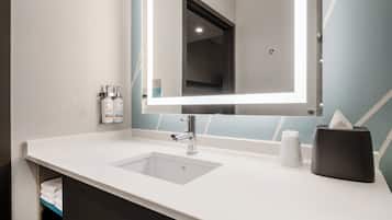 A modern bathroom with a white sink, a mirror, and a towel dispenser.