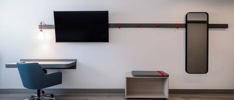 Un espacio de oficina moderno con una televisión de pantalla plana montada en la pared, un escritorio con una silla y una pequeña estantería con un cojín.