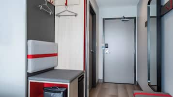 Una habitación de hotel con cama, un escritorio pequeño con silla, armario, espejo y puerta.