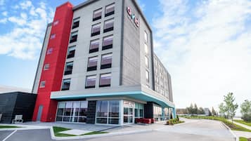 Edificio de hotel moderno con una fachada destacada en rojo y gris, amplias ventanas y un área exterior bien cuidada con asientos.
