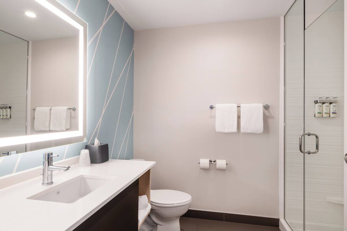A modern bathroom with a large mirror, a sink, a toilet, and a glass shower enclosure.