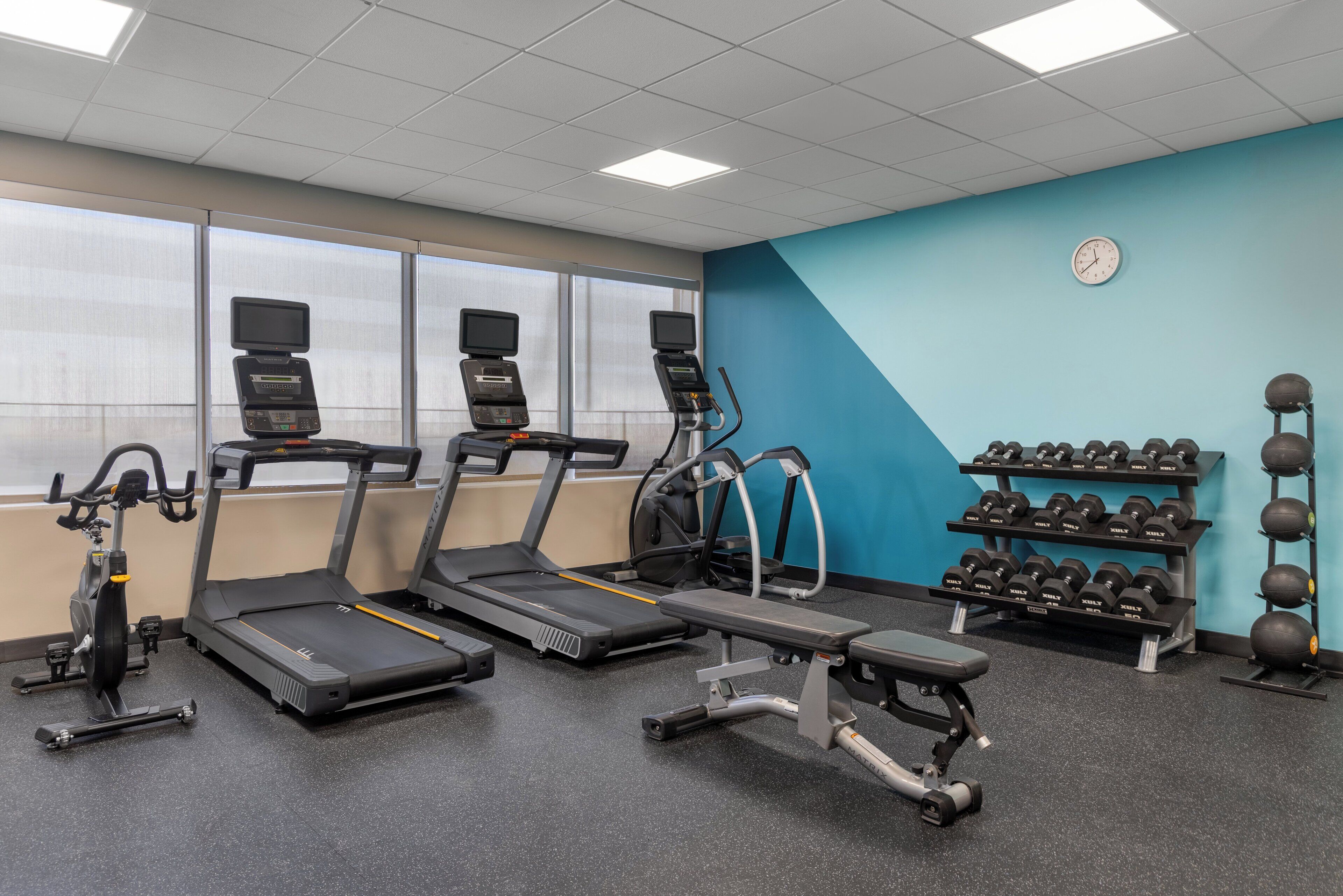 A gym with treadmills, an elliptical, a bench press, and a rack of dumbbells.