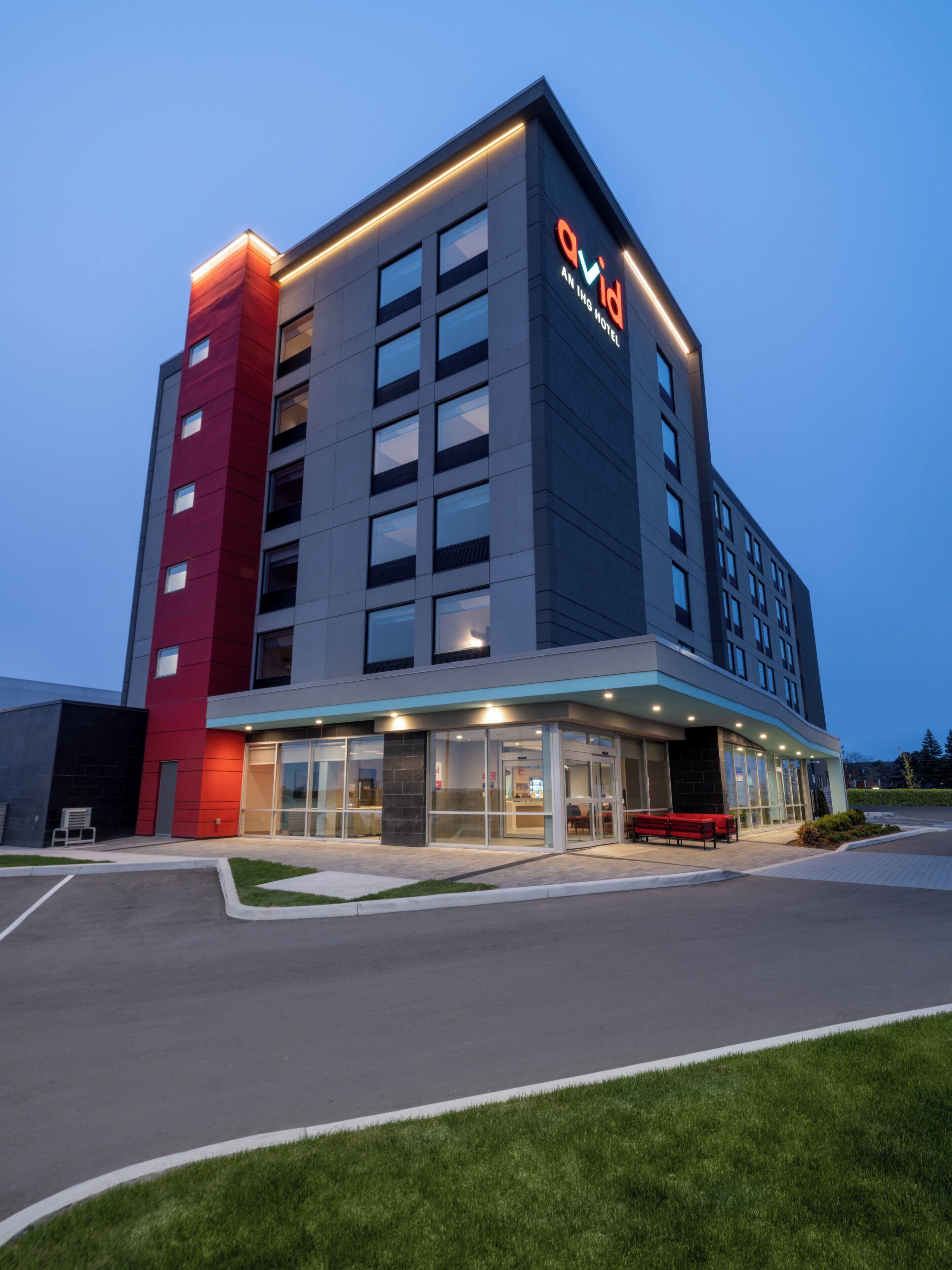 A modern hotel building with a prominent 'QVIID' sign, a glass entrance, and a red accent wall.