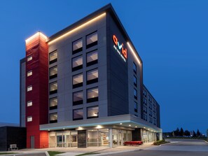 A modern hotel building with a prominent 'QVI' sign, multiple floors, and a well-lit entrance.