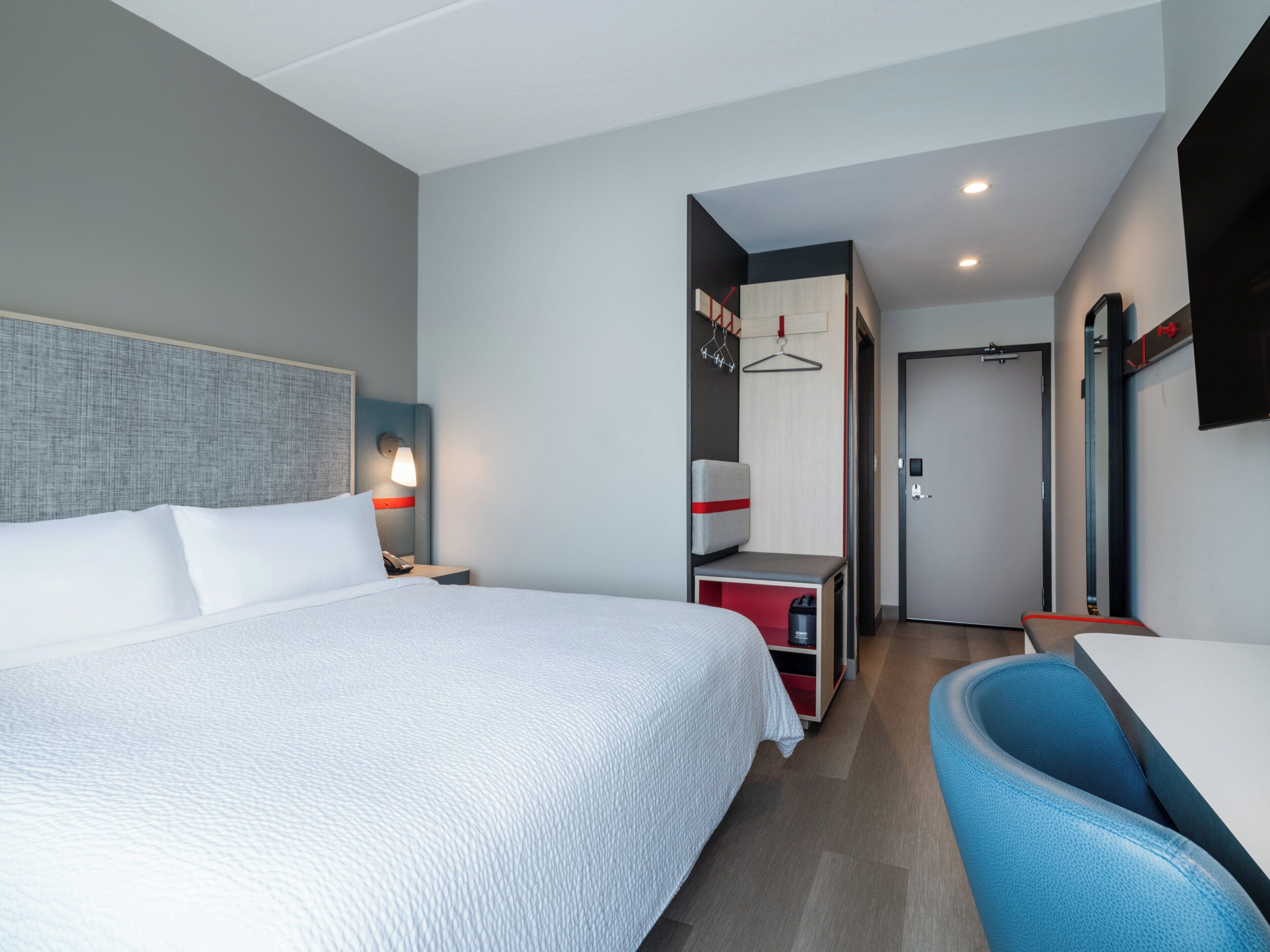 A modern hotel room with a large bed, a desk, and a chair.