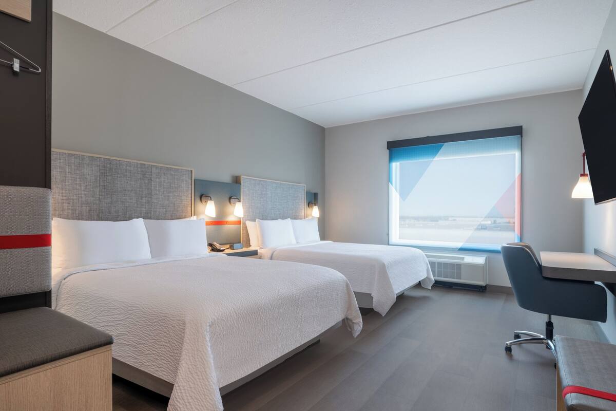 A hotel room with two beds, a desk, and a TV.