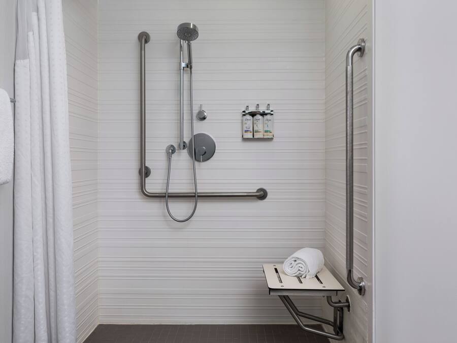 A bathroom with a shower, grab bars, a towel rack, and a toilet with a raised seat.
