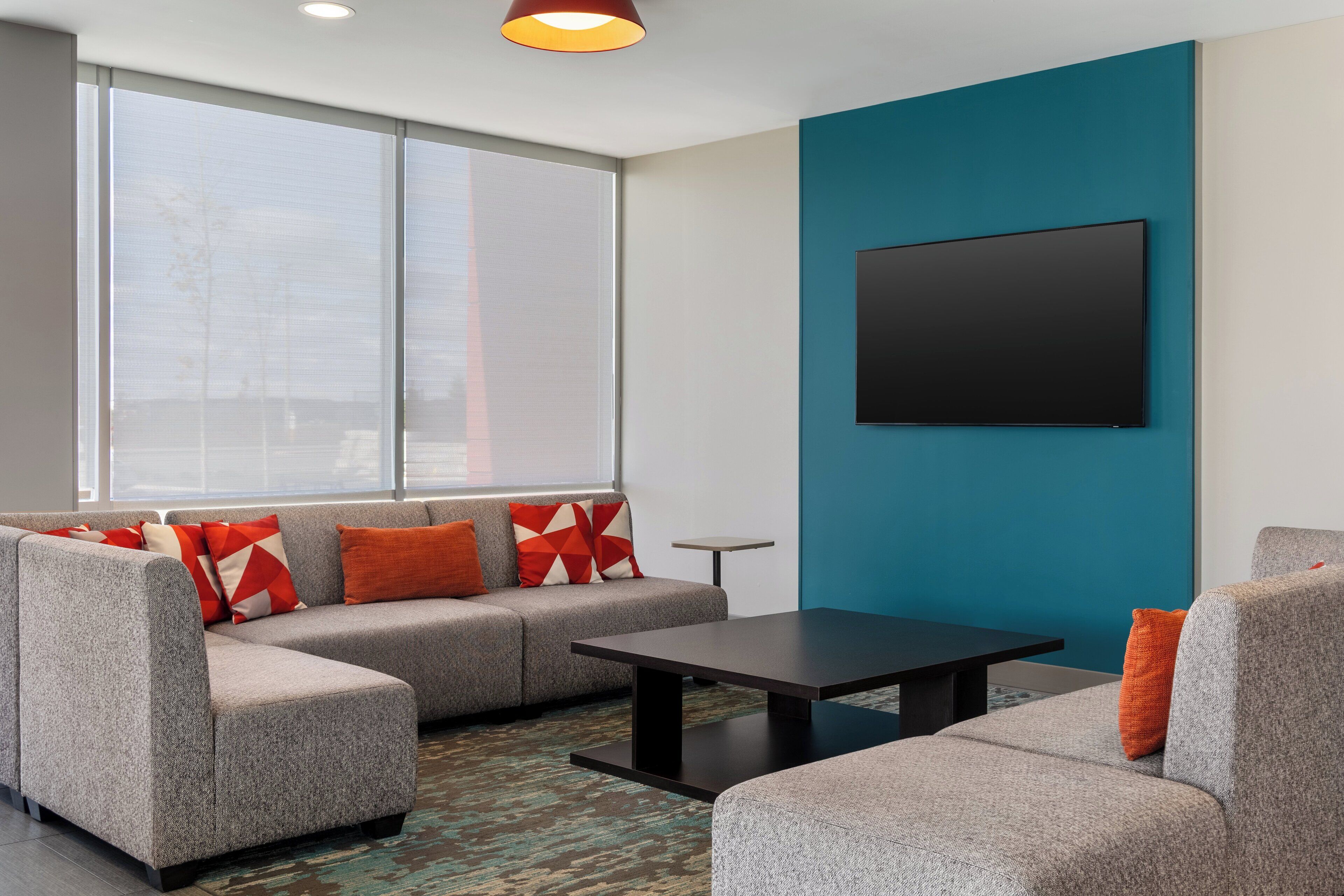 A modern living room with a sectional sofa, a coffee table, and a flat-screen TV mounted on a teal wall.